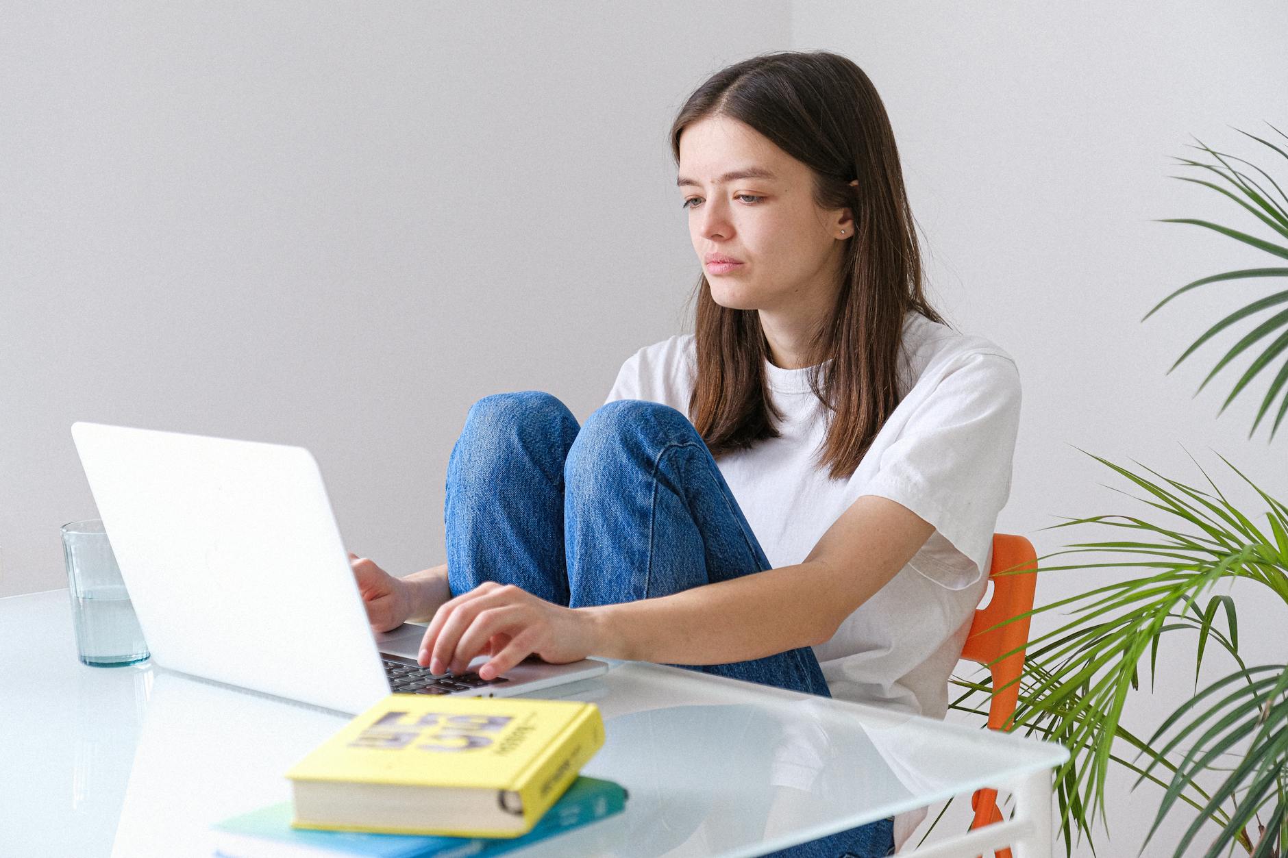woman in white crew neck t shirt and blue denim jeans working on a laptop